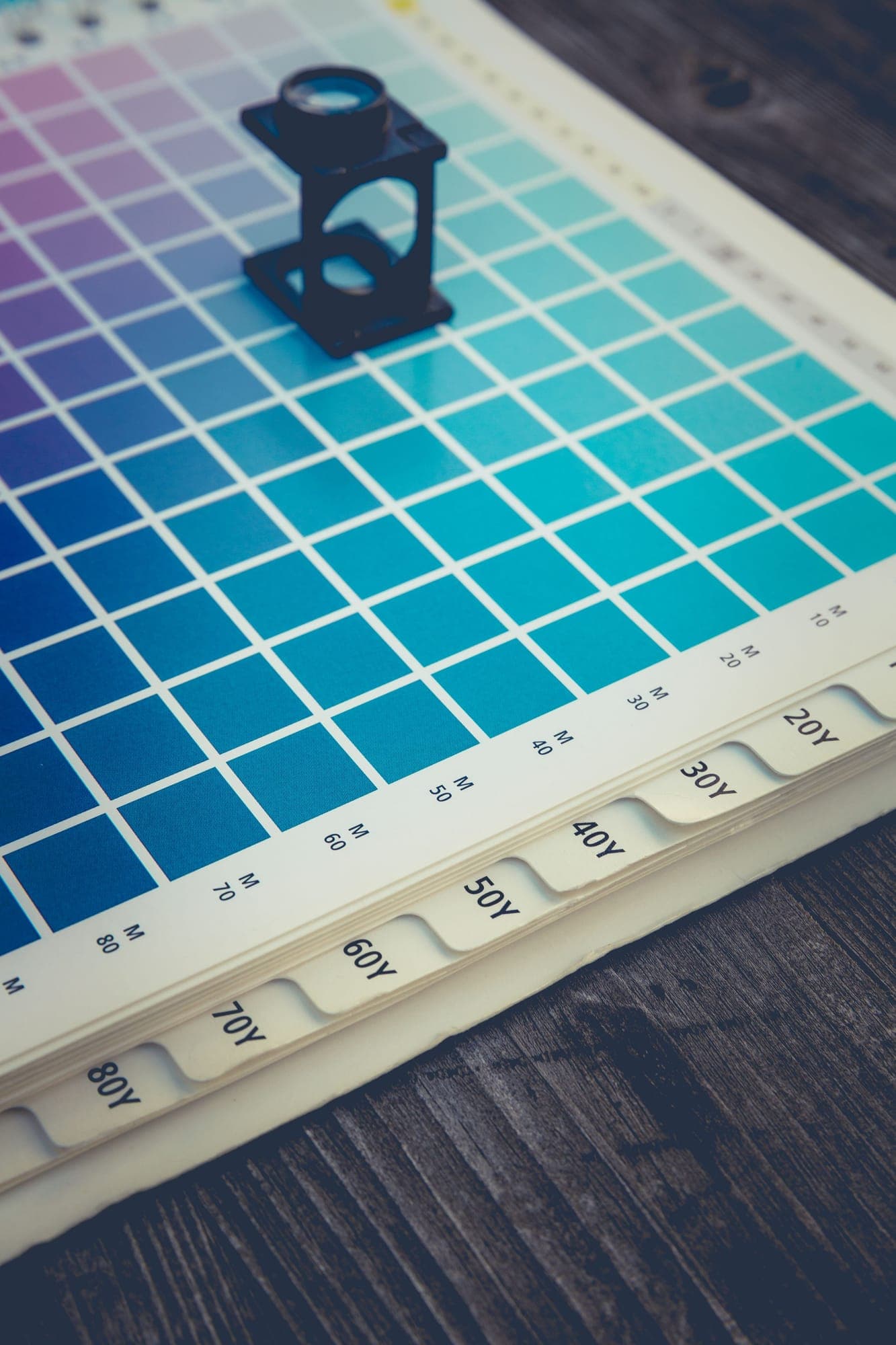 A hand checking a printed color proof on a wooden table
