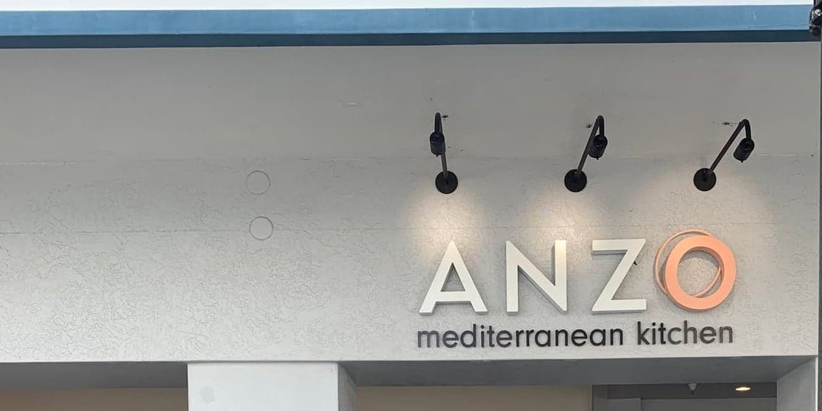 Dimensional letters lit by gooseneck lamps over a restaurant entrance