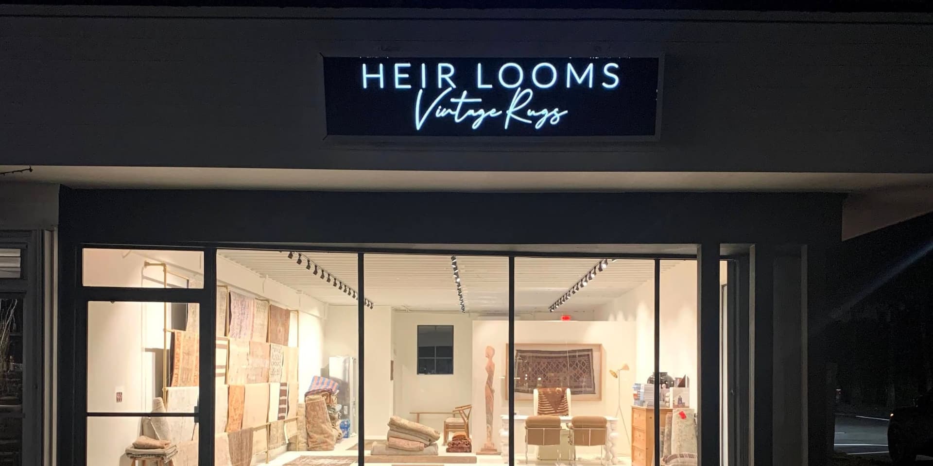 An illuminated sign over a rug gallery storefront at night